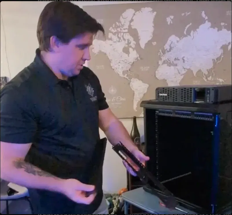 Chris Creamer, founder of Tessellate Systems, in a black Tessellate polo standing at a server rack with a world map behind him