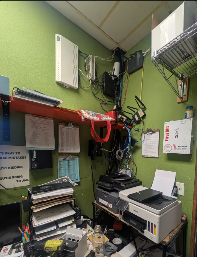 Before: tangled consumer networking gear and cables on a green back-office wall at Fibber Magee's Irish Pub